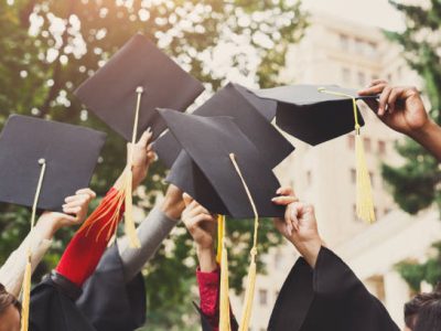 A group of multietnic students celebrating their graduation by throwing caps in the air closeup. Education, qualification and gown concept.