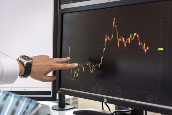 Detailed view of a hand pointing at a cryptocurrency trading graph on a monitor.