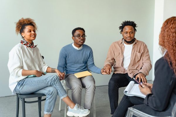 A diverse group of adults in a supportive therapy session, holding hands indoors.