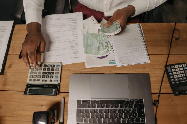 Close-up of a person counting cash with documents and a laptop in an office setting.