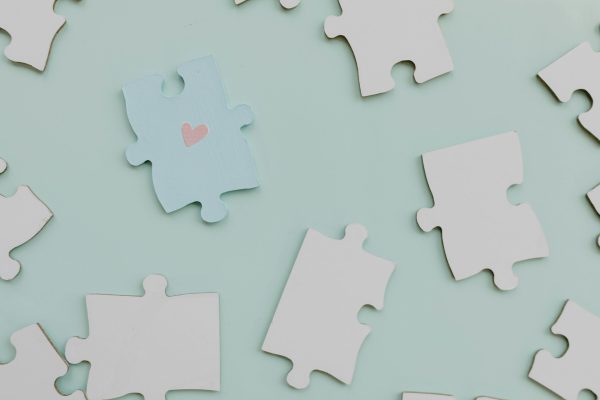 Top view of jigsaw puzzle pieces on a calm green background with a heart on one piece.